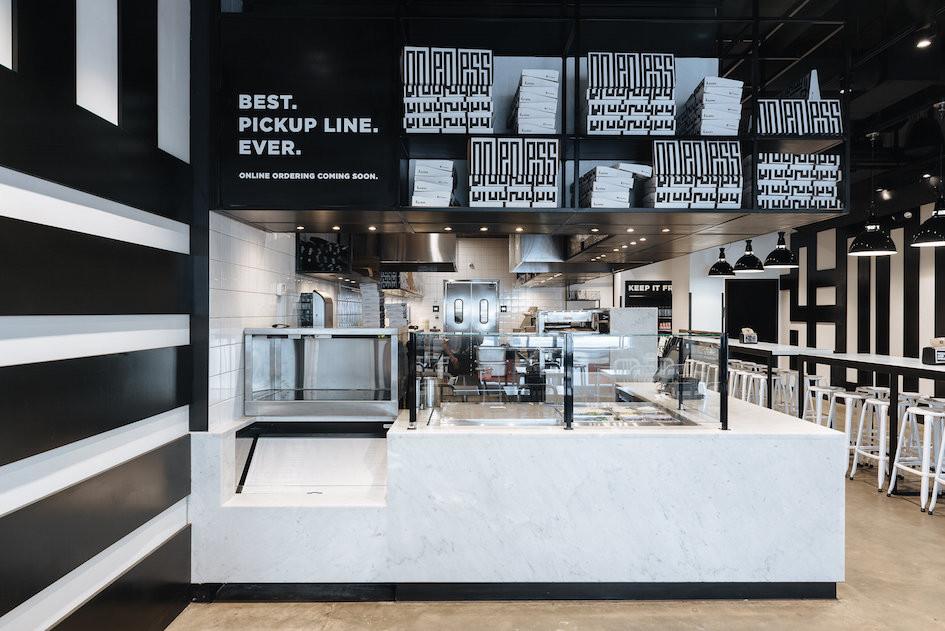 &pizza interior with marble pickup counter, glass barrier, stacked pizza boxes, and sign reading BEST. PICKUP LINE. EVER.