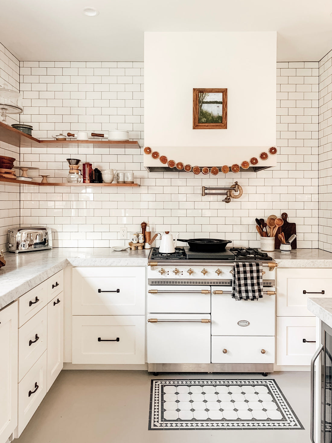Bright farmhouse kitchen with white subway tile, open wood shelves, a white range with brass accents, and dried orange slice garland