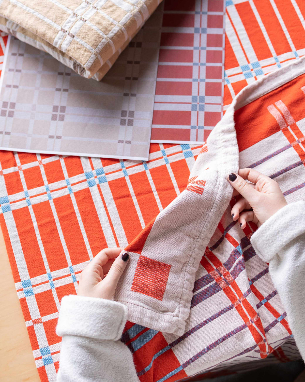 Close up of Shelburne cotton coverlet showing orange and cream plaid and woven texture with hands holding corner