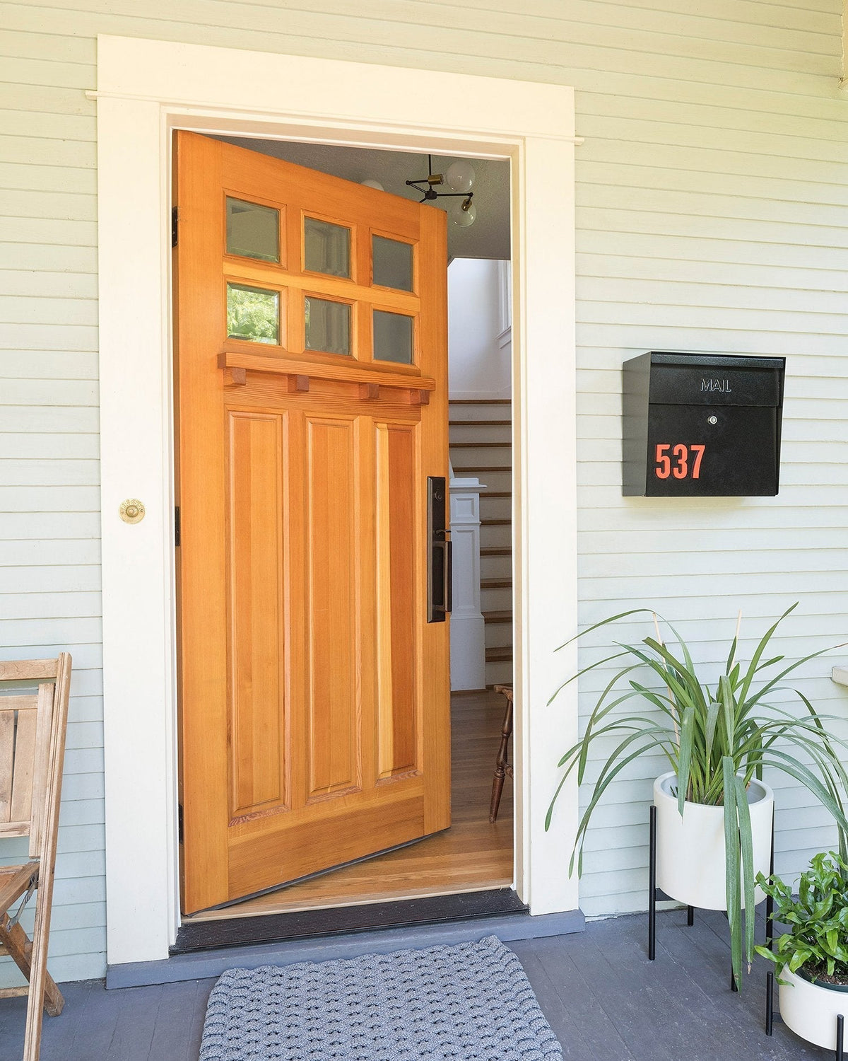 Open wooden front door with black handle revealing an interior stair and a black mailbox marked 537 on light-gray porch siding
