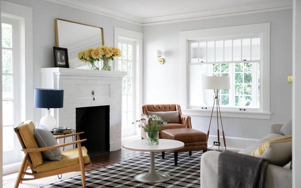 Staged living room with fireplace and seating grouped around a round coffee table, natural light from large windows and neutral gray walls