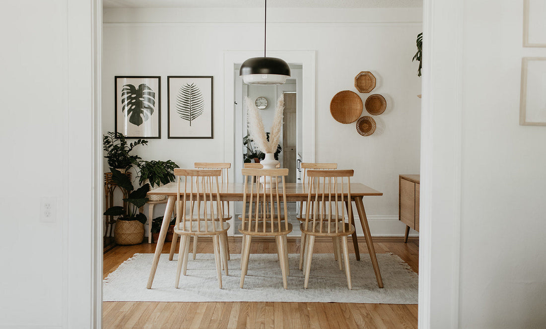 Dining room with wooden table and six spindle-back chairs, black pendant light, framed botanical prints, woven wall baskets, and potted plants