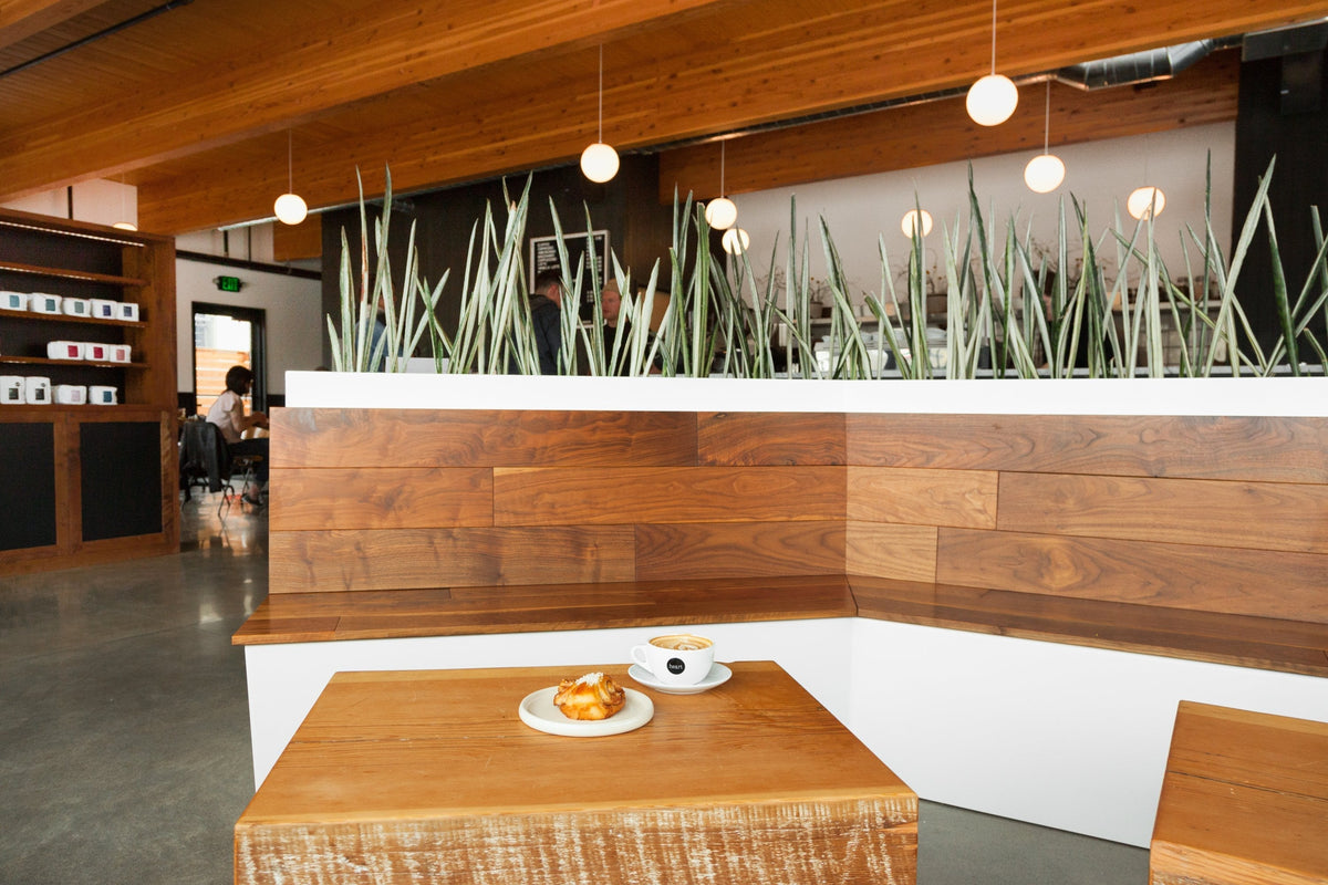 Cafe corner with wooden bench and planter, small table in foreground holding a latte in a Heart Roasters cup and a pastry