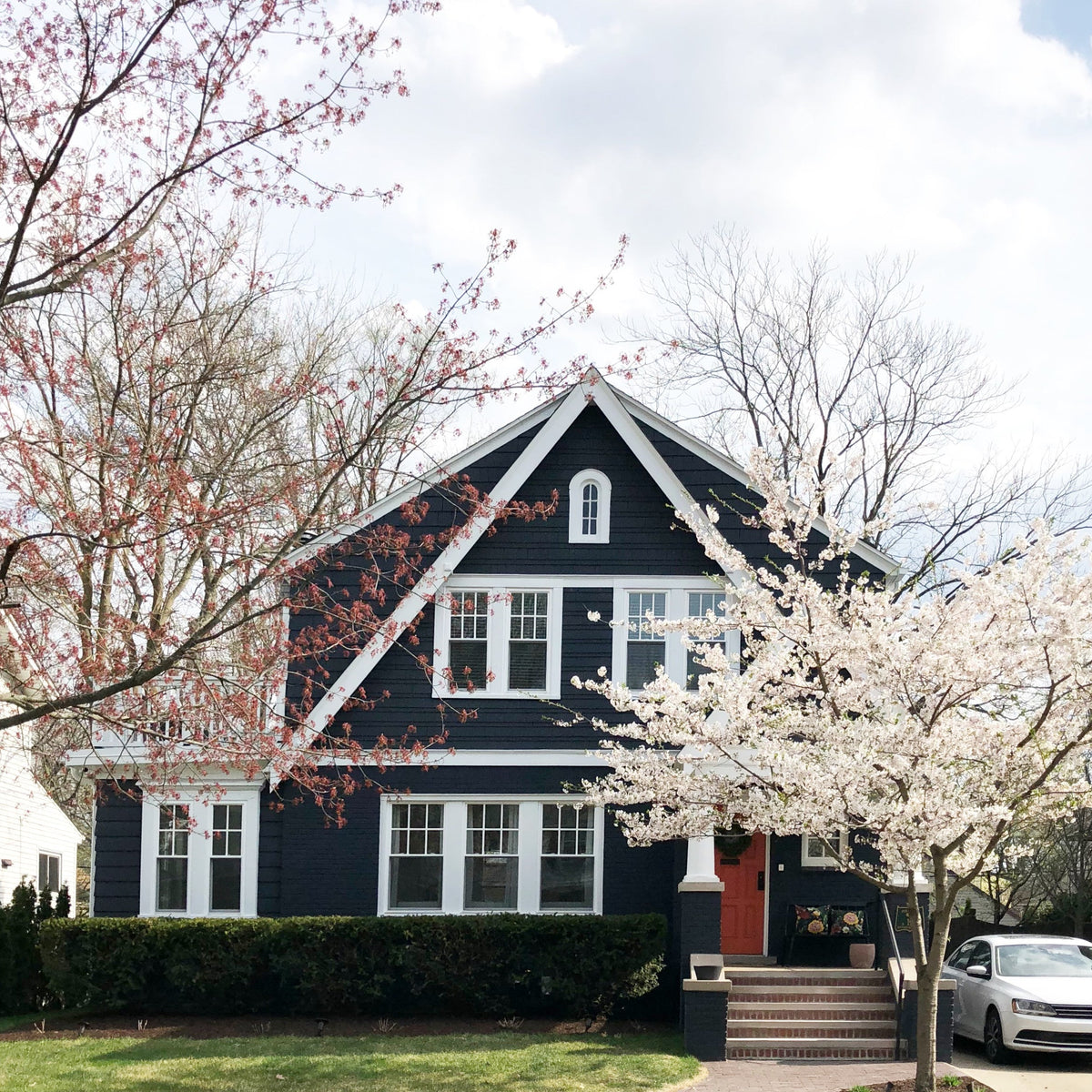 Front exterior of a navy house with white trim and red door framed by blooming pink and white spring trees
