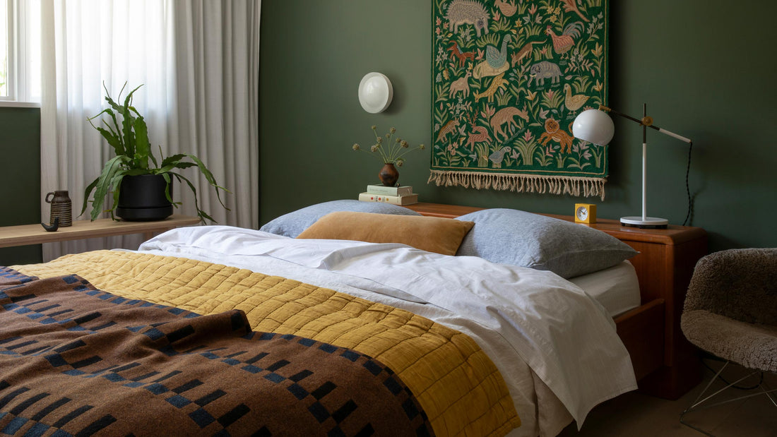 Bed and bedside area featuring a round white wall sconce mounted above a mid-century nightstand against a deep green wall
