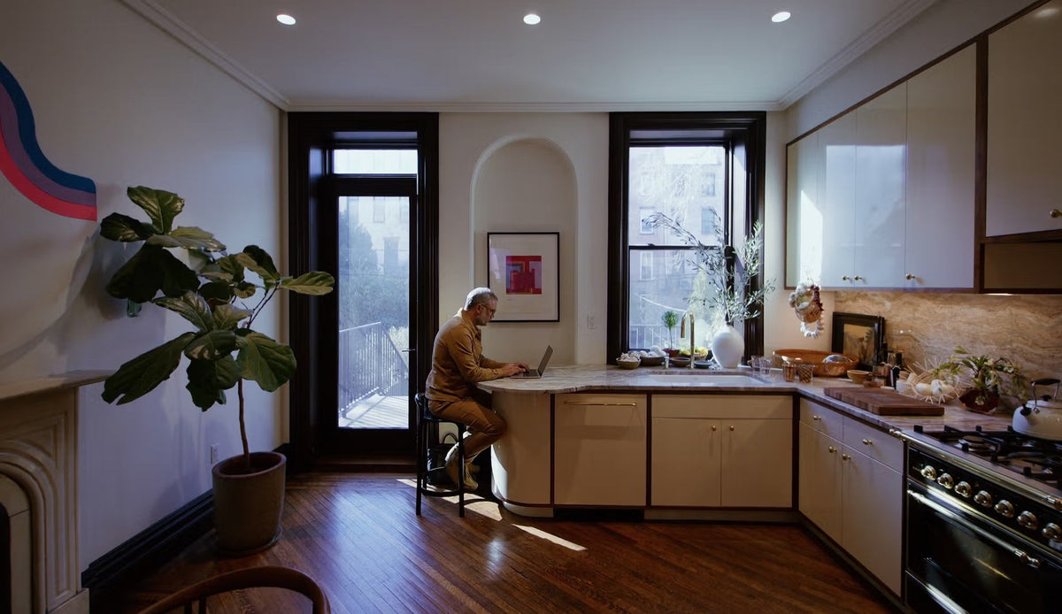 Apartment kitchen with large windows and man sitting at countertop working on laptop