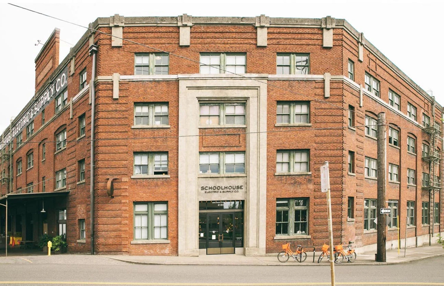 Exterior of the Schoolhouse brick building at a street corner showing the main entrance and parked bicycles