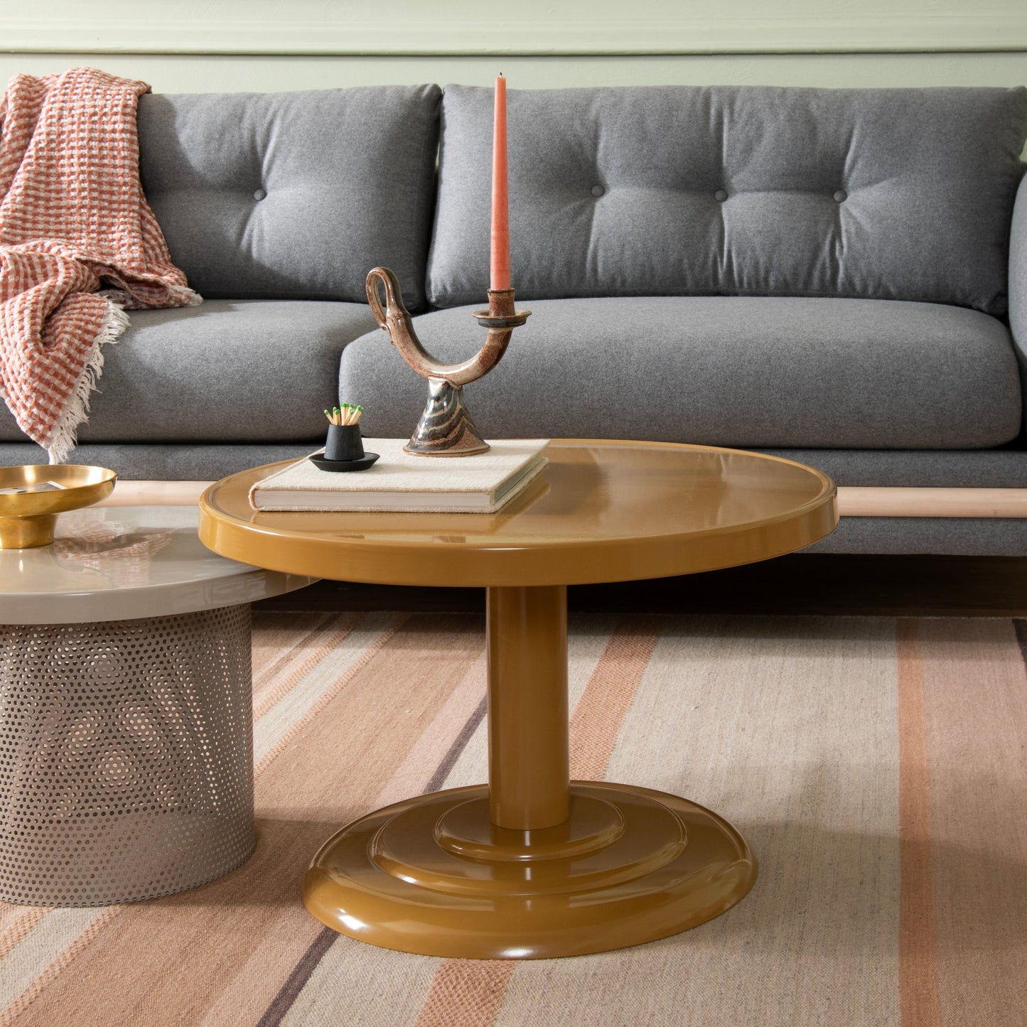 Front view of Owen Cocktail Table showcasing mustard-gloss round top and pedestal base with gray tufted sofa background