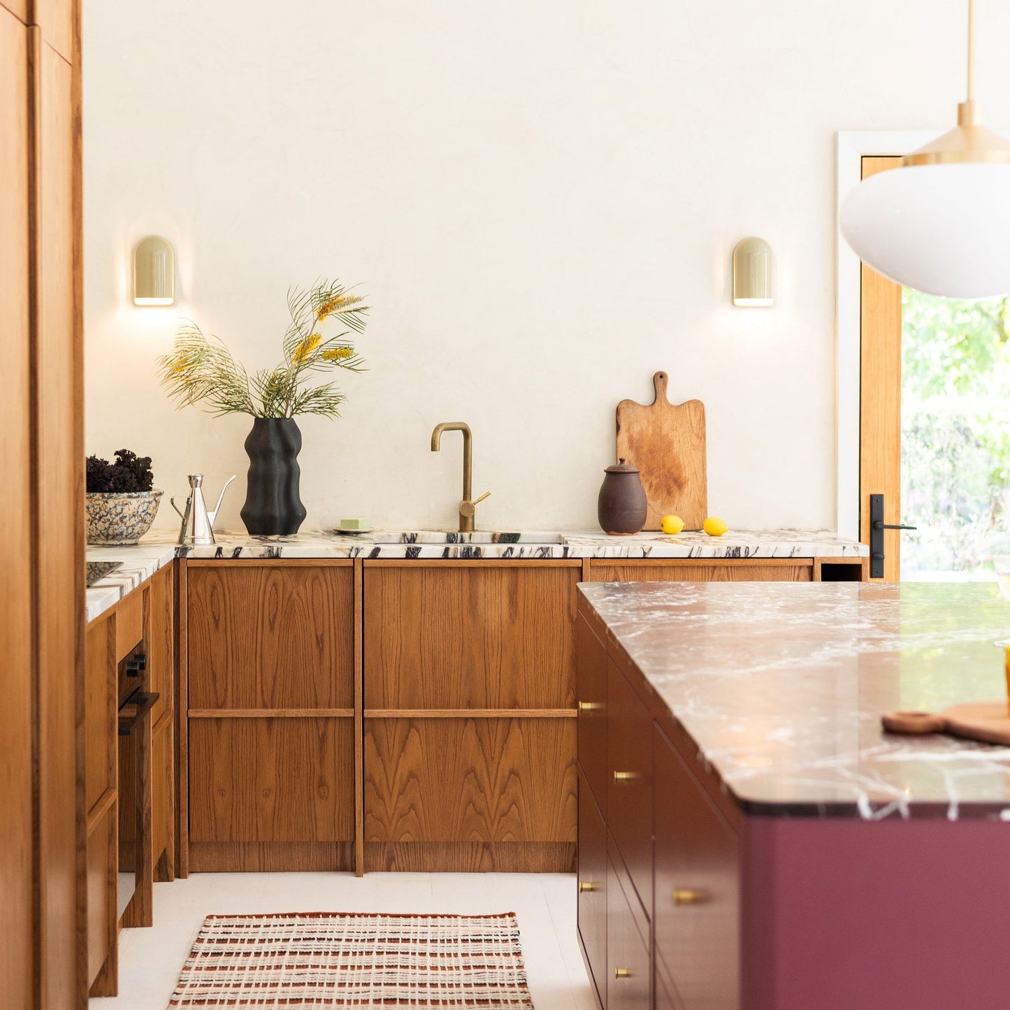 Two Allegheny Slim Sconces mounted on a kitchen wall, softly lit above a marble countertop with wooden cabinets