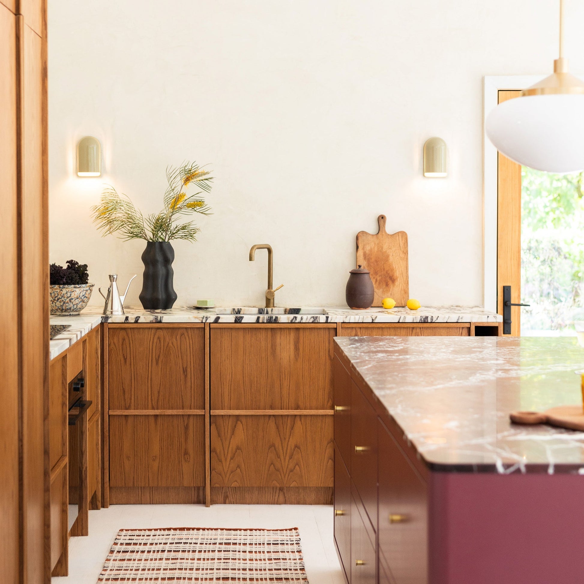 Two Allegheny Slim Sconces mounted on a kitchen wall, softly lit above a marble countertop with wooden cabinets