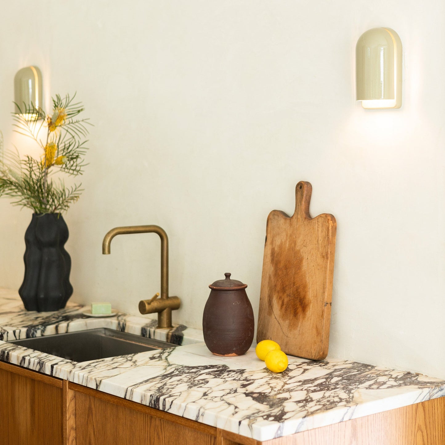 Right view of Allegheny Slim Sconce with glossy rounded shade casting downward light over a marble kitchen counter and brass faucet