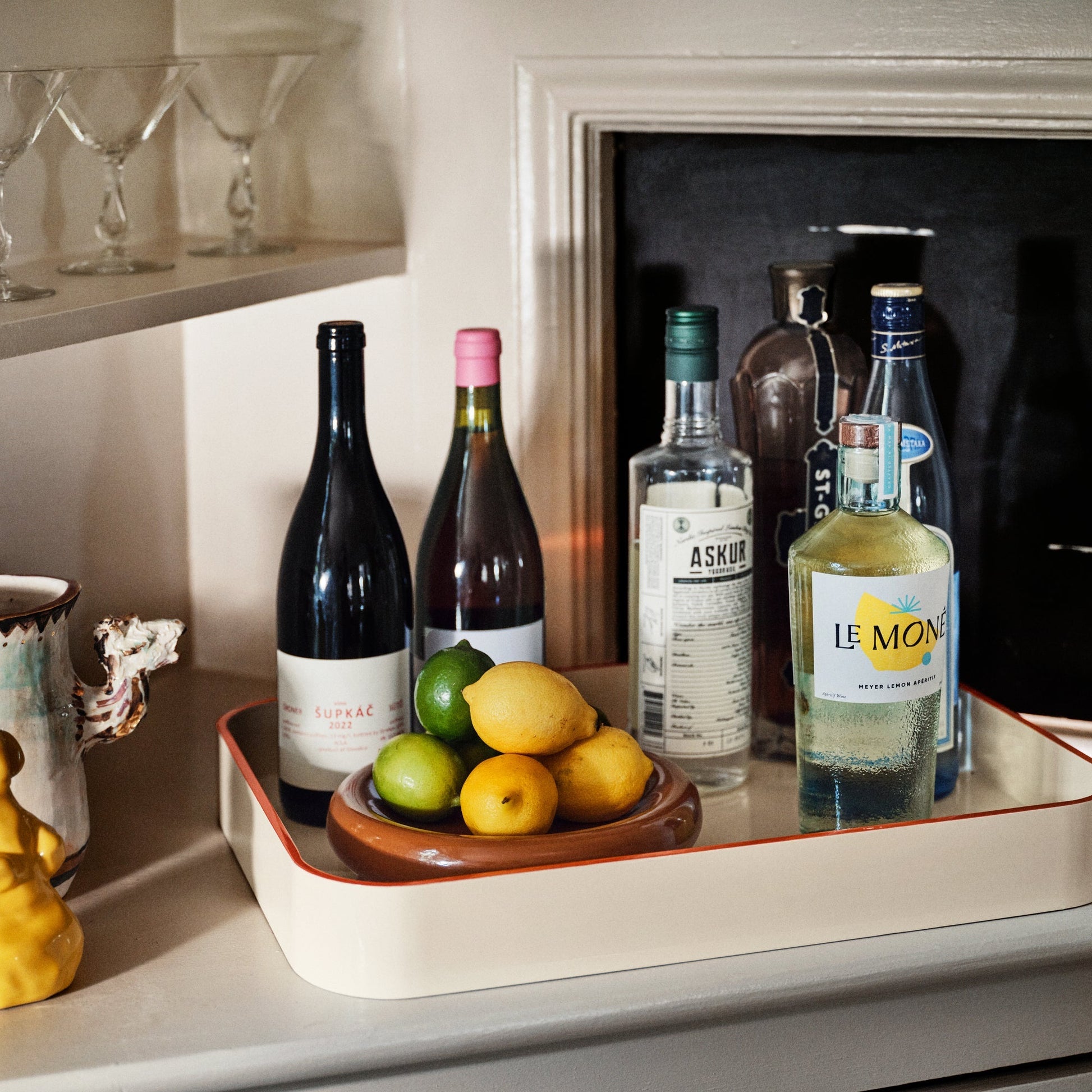 Angled view of Yves cast metal catch all showcasing a glossy raisin rim and shallow tray holding bottles and lemons and limes on a shelf