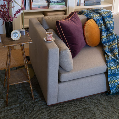 Angled view of Velvet Piped Pillow showcasing raisin cotton velvet with contrast rust piping on a gray sofa