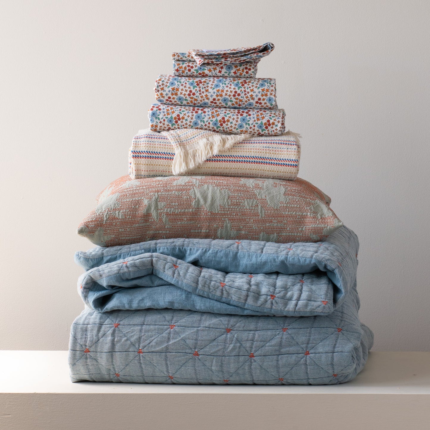 Front view of folded Peak Stitch duvet showcasing blue and orange floral print and quilted peak-stitch detail on stacked bedding against a pale wall