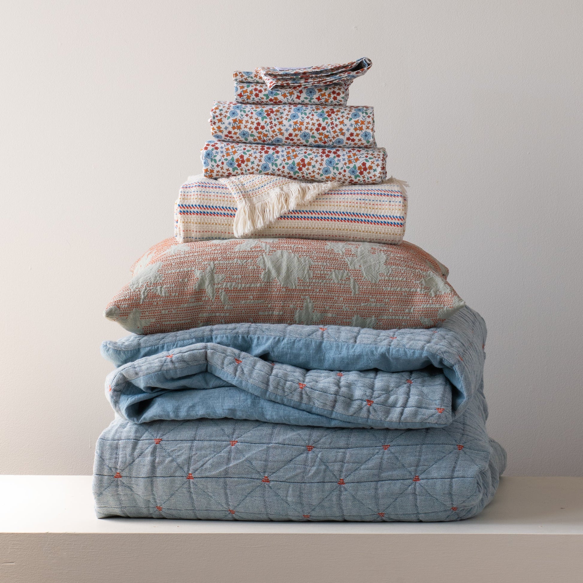 Front view of folded Peak Stitch duvet showcasing blue and orange floral print and quilted peak-stitch detail on stacked bedding against a pale wall