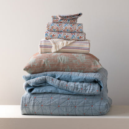 Front view of folded Peak Stitch duvet showcasing blue and orange floral print and quilted peak-stitch detail on stacked bedding against a pale wall