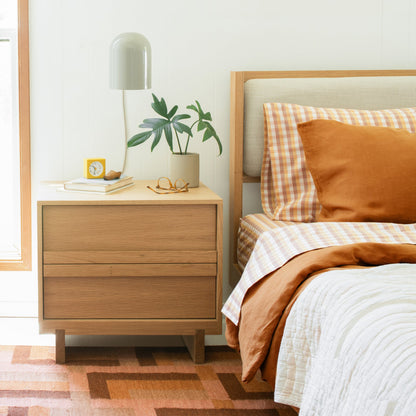 Allegheny 6-inch plug-in sconce above a nightstand in a bright bedroom with oak headboard, plaid bedding, plant, and yellow alarm clock