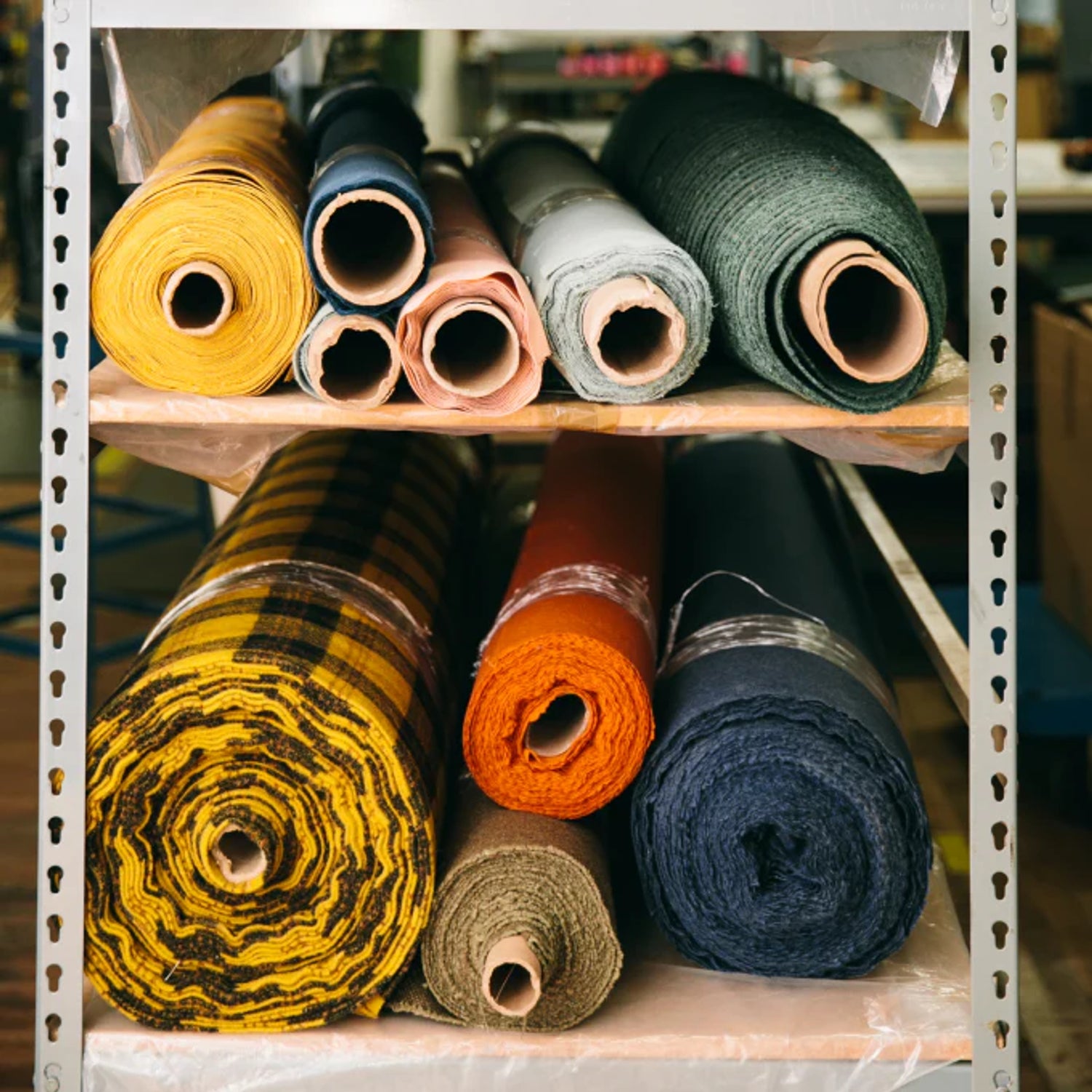 Rolls of upholstery fabric on metal shelving in a workshop, assorted colors and textures
