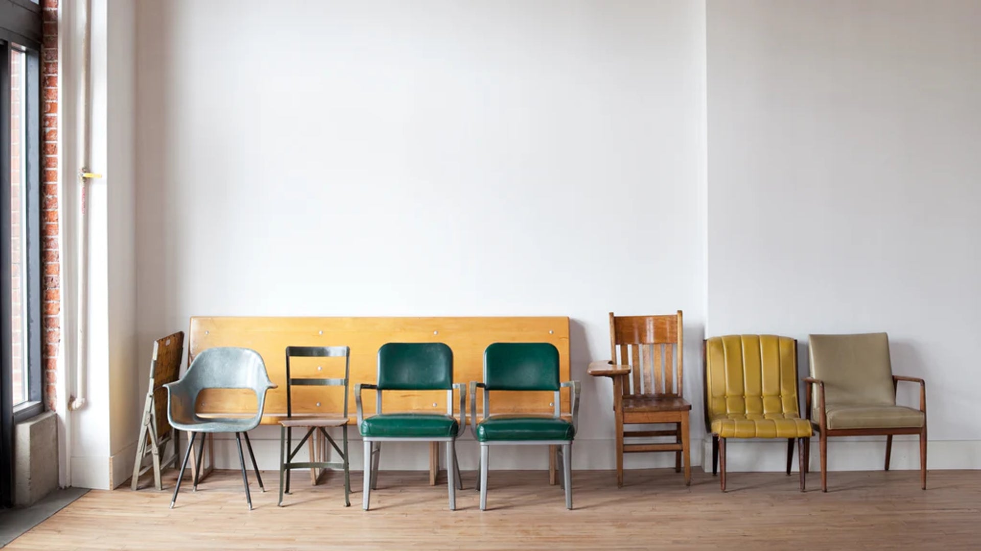 Mismatched chairs lined up against a white wall in a sunlit room