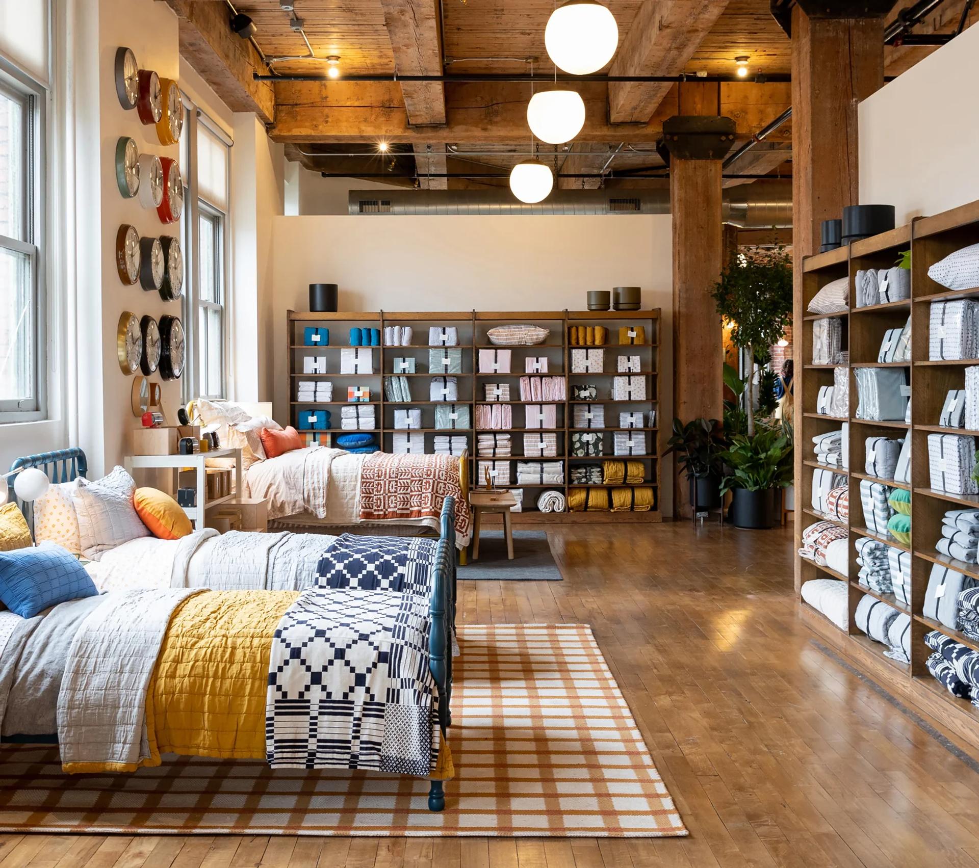 Loft-style Schoolhouse showroom with styled beds, wall clocks, and shelving of folded bedding and pillows