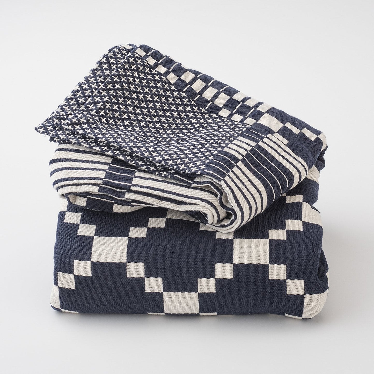 Folded Winter and Summer Cotton Coverlet showing navy and white woven geometric and striped patterns on white background