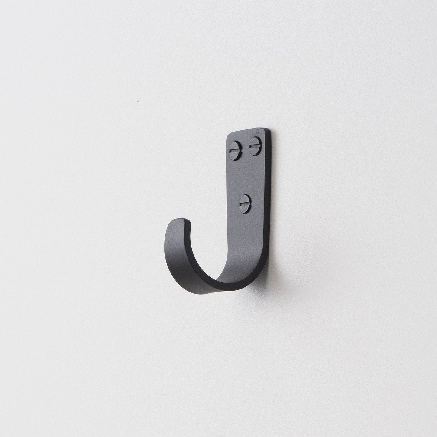 Angled close-up of Thomas Hook showing J-shaped metal hook with exposed screw heads on a white wall