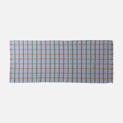 Top-down view of Cotton Grid Flatweave Rug showcasing lavender field with green and tan grid lines and fringed edge on white background