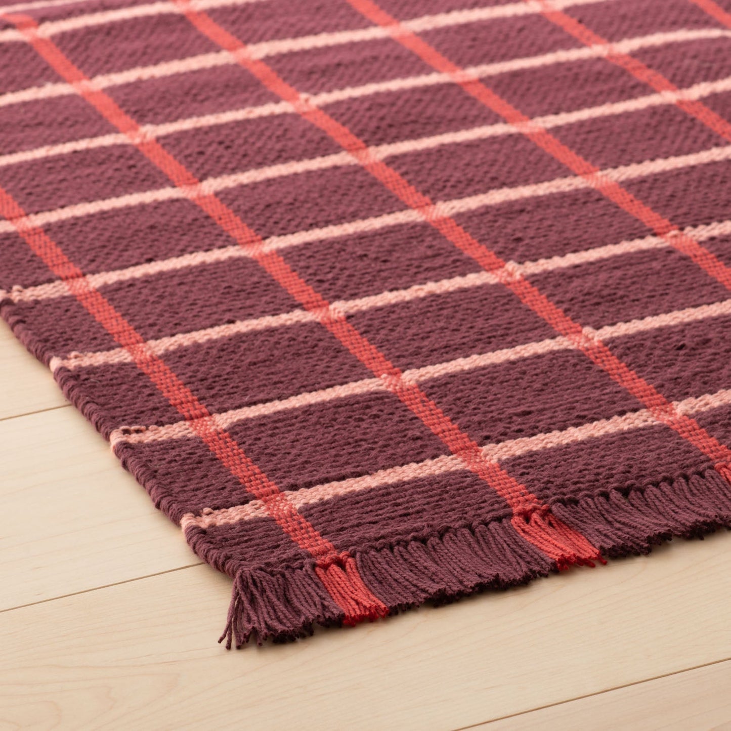 Angled close-up of Cotton Grid Flatweave Rug showing large grid pattern, flatwoven texture, and fringed edge on light wood floor