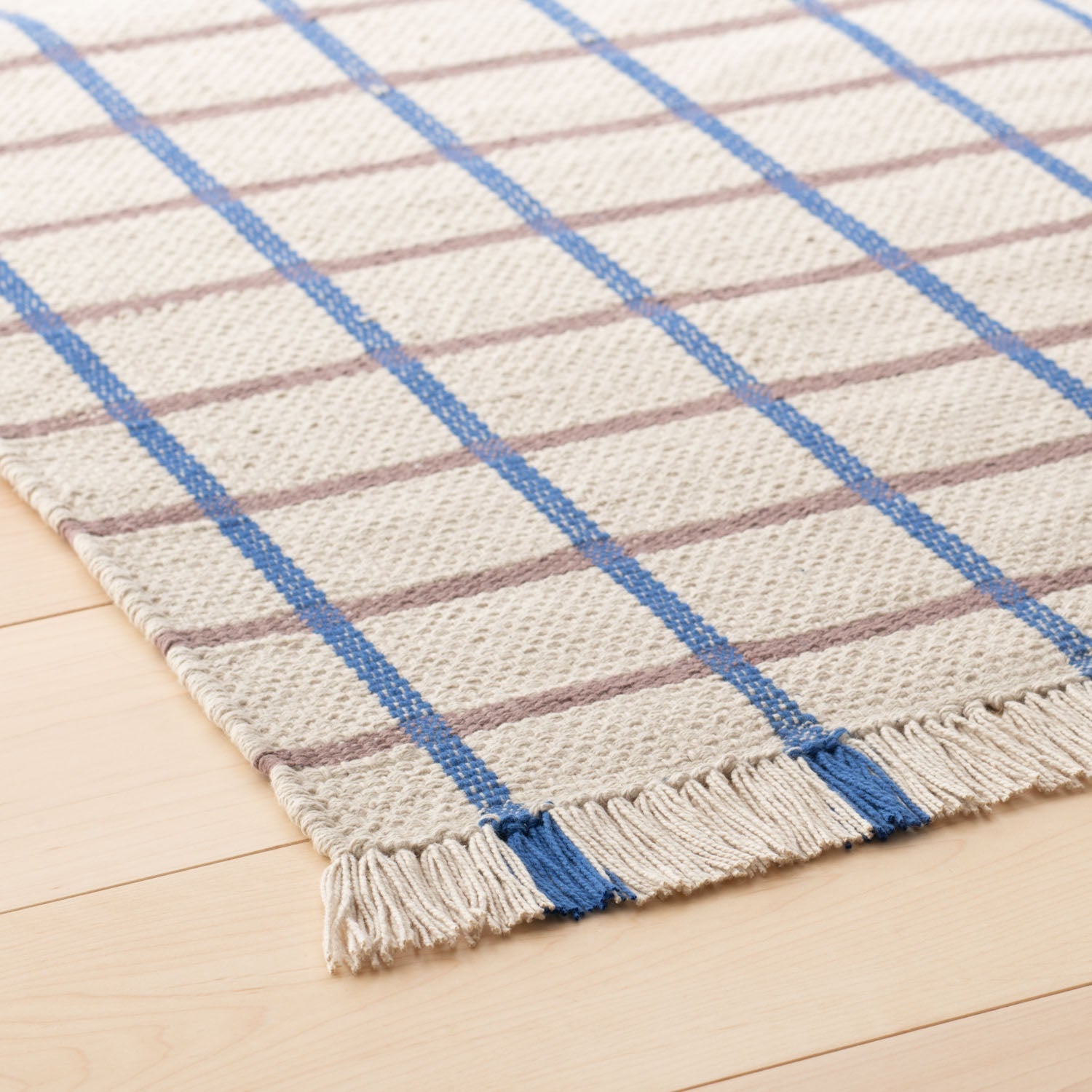 Close-up of Cotton Grid Flatweave Rug showing cream woven texture, blue and taupe grid lines and fringe on light wood floor