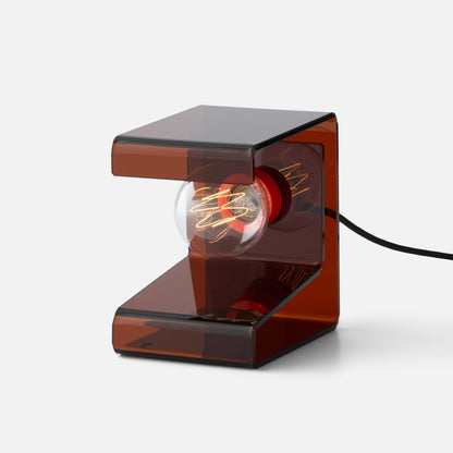 Three quarter close up of Pop Light II table lamp showcasing amber translucent acrylic body and exposed filament bulb on light gray background