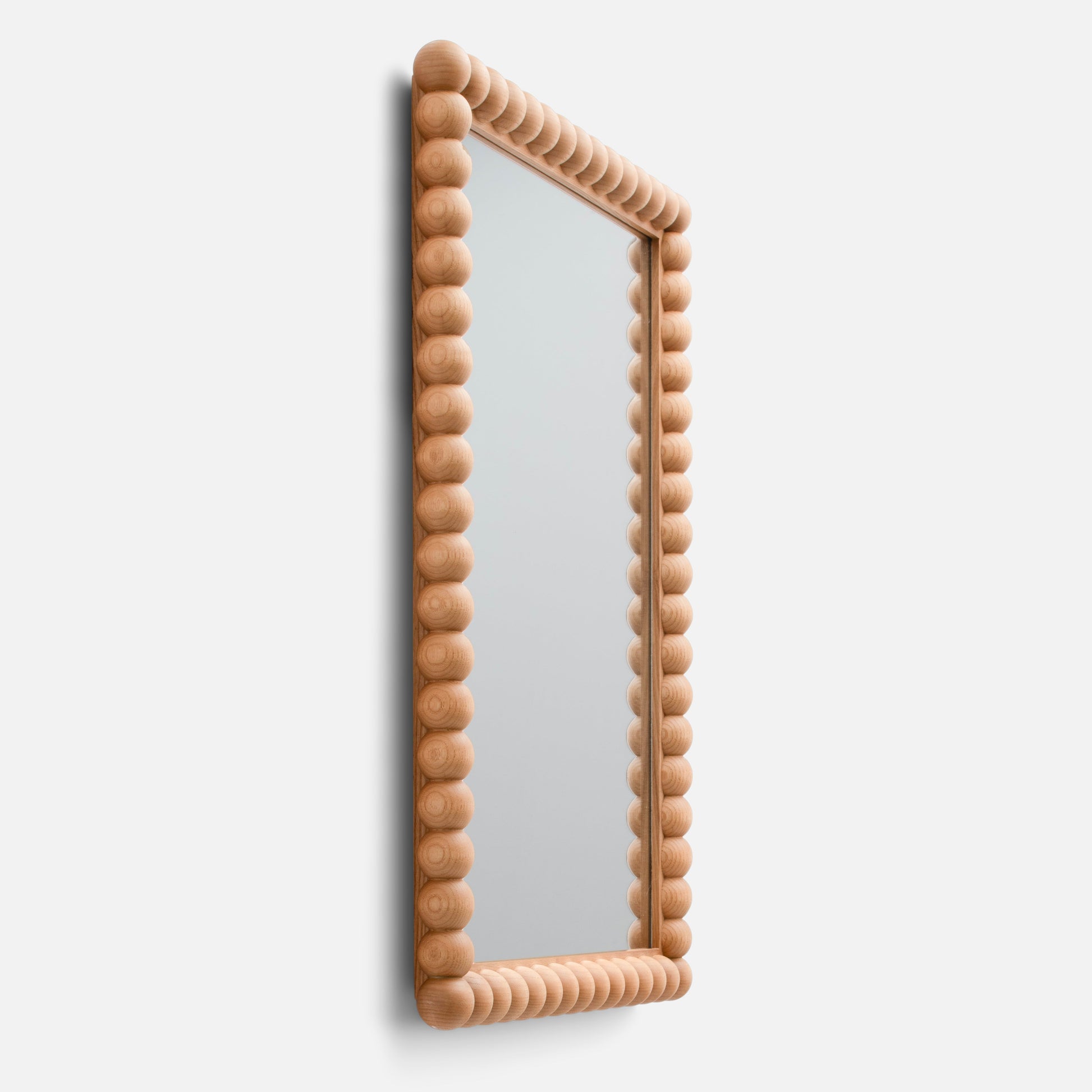 Angled side view of Bobbin Mirror showing ash wood beaded frame and rectangular mirror against a white background