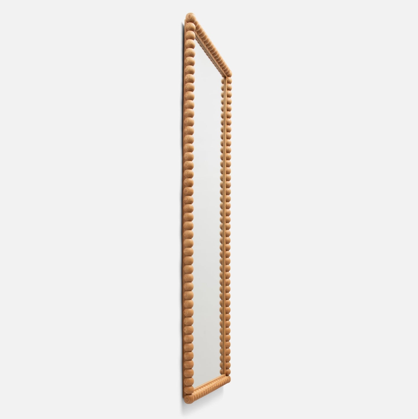 Three-quarter side view of Bobbin Mirror showcasing turned-wood bobbin frame in ash finish against a light background