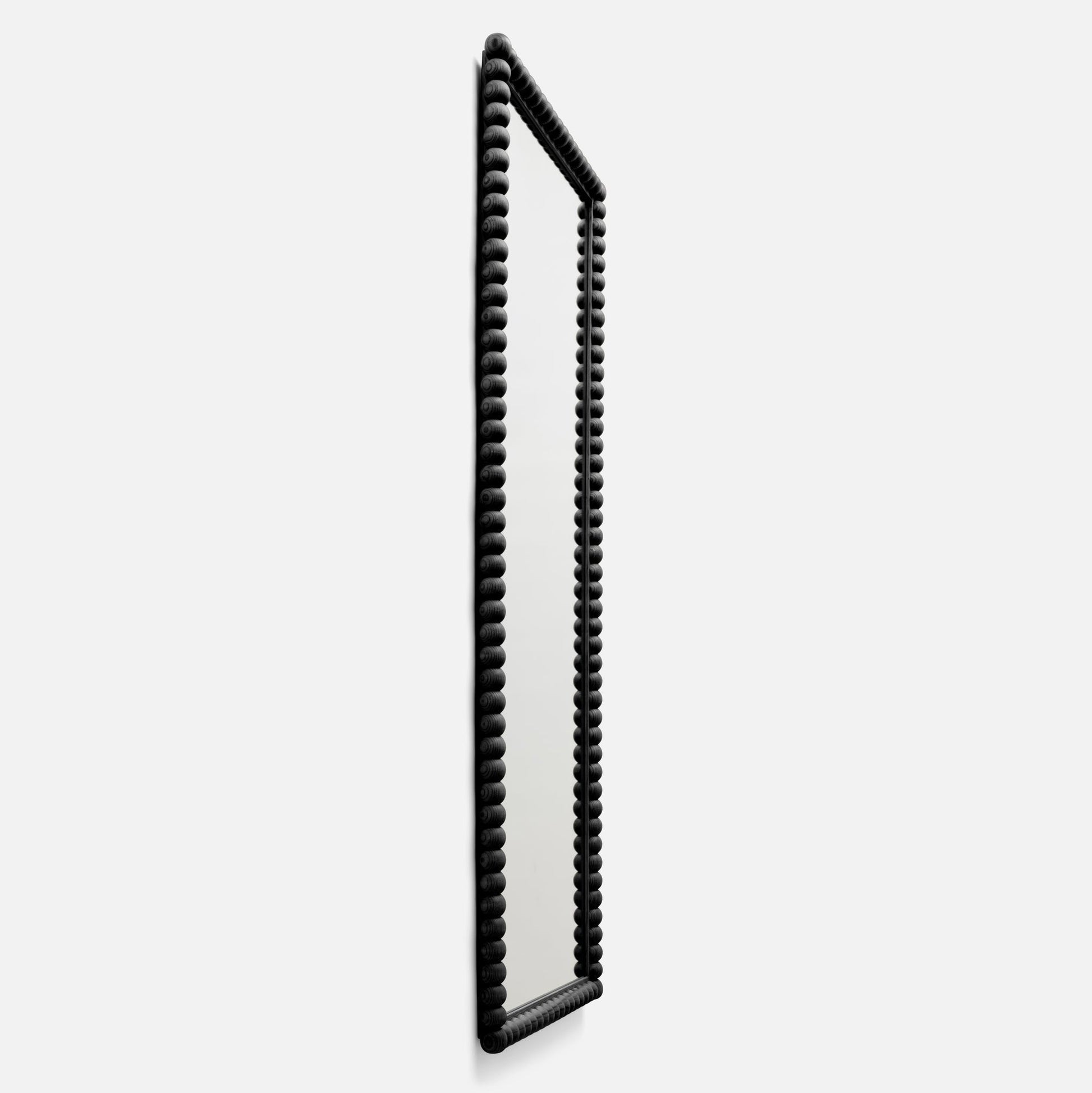 Angled side view of Bobbin Mirror, 28 x 68 in, showing black beaded wood frame and full-length mirror on white background