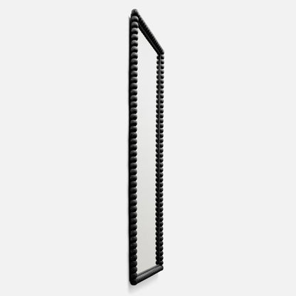 Angled side view of Bobbin Mirror, 28 x 68 in, showing black beaded wood frame and full-length mirror on white background