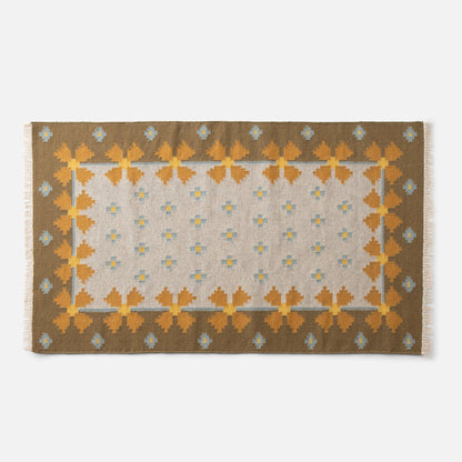 Top-down corner of Flora Wool Flatweave Rug showing flatweave wool texture and mustard-and-blue floral border on white background