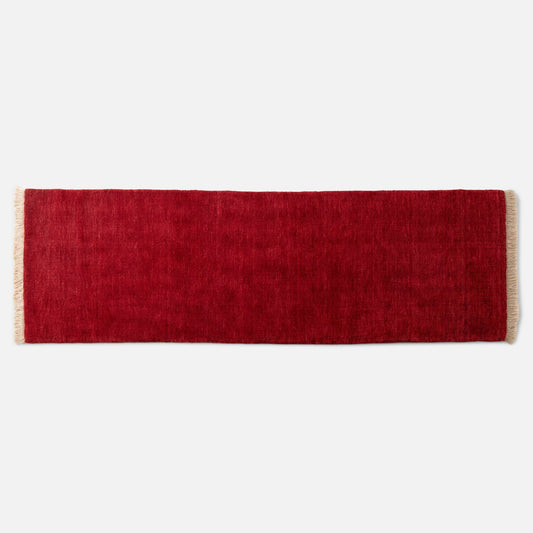 Top edge of Mesa Wool Rug showcasing deep red hand-loomed wool pile and cream fringe on light gray background