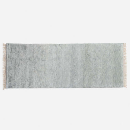 Top-down view of green Mesa Wool Rug showcasing hand-loomed cut pile and tasseled fringe on a white studio background