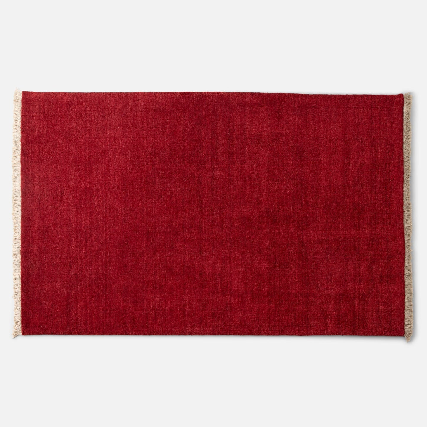 Top-down close-up of Mesa Wool Rug showing deep red hand-loomed wool pile and natural fringe against white background