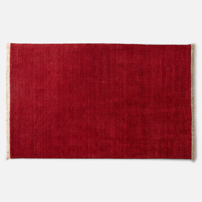Top-down close-up of Mesa Wool Rug showing deep red hand-loomed wool pile and natural fringe against white background