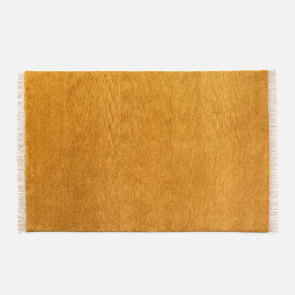 Top view of Mesa Wool Rug showcasing golden hand-loomed cut pile and ivory fringe on white background