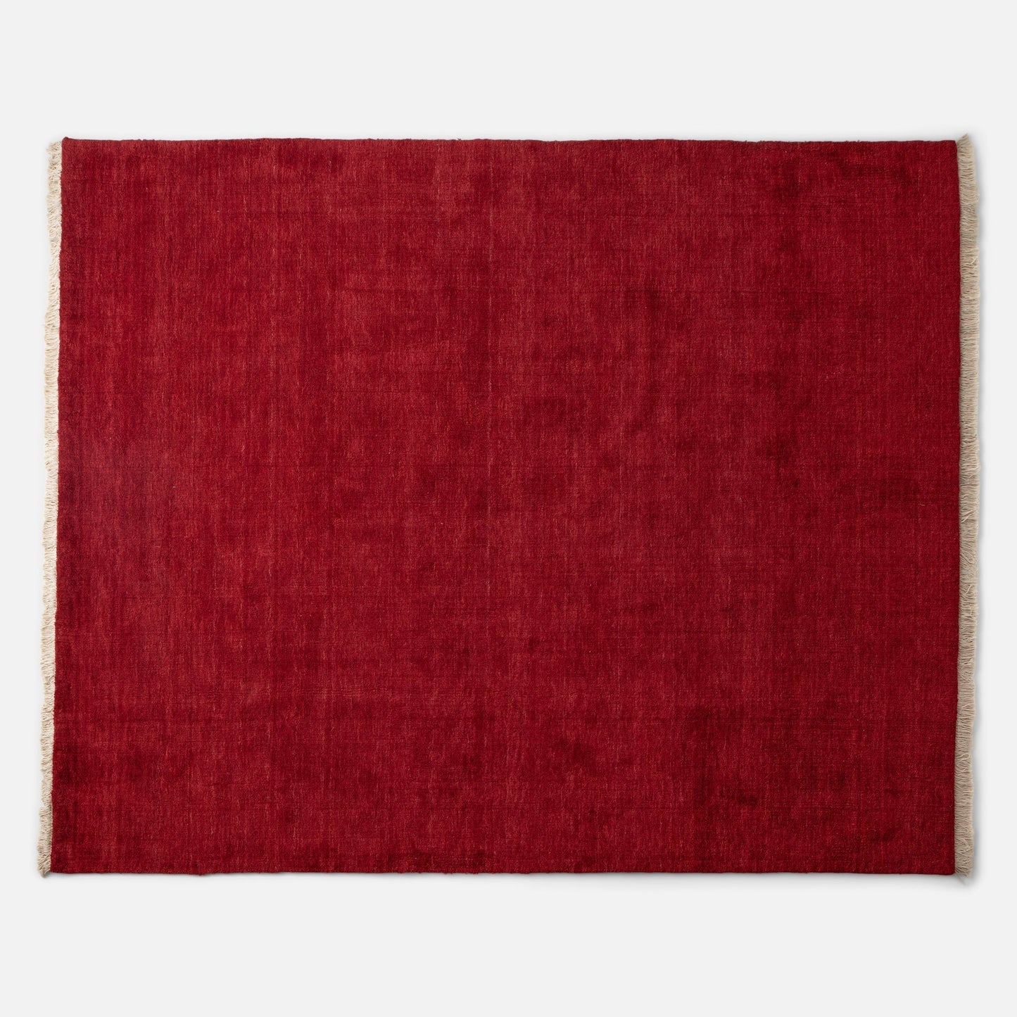 Top edge view of Mesa Wool Rug showcasing red hand-loomed wool pile and natural fringe on a white background