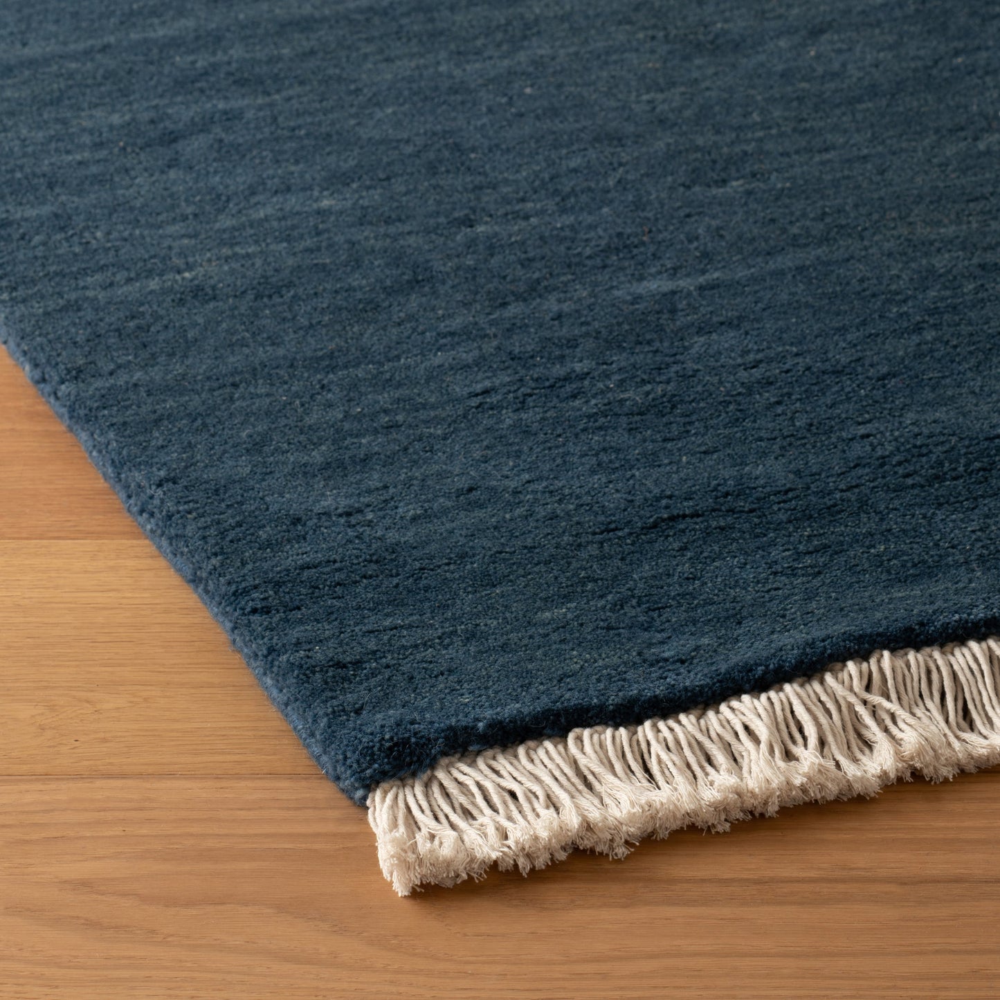 Close-up of corner of Mesa Wool Rug showcasing hand-loomed wool pile and fringe on a hardwood floor