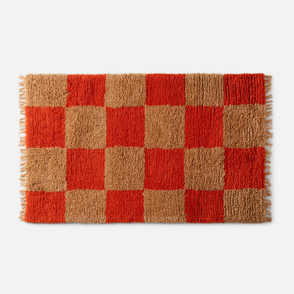 Close-up of top edge of Schoolhouse x Clare V. Jacques shag wool rug showcasing high-pile orange and tan checker squares and fringe on white background