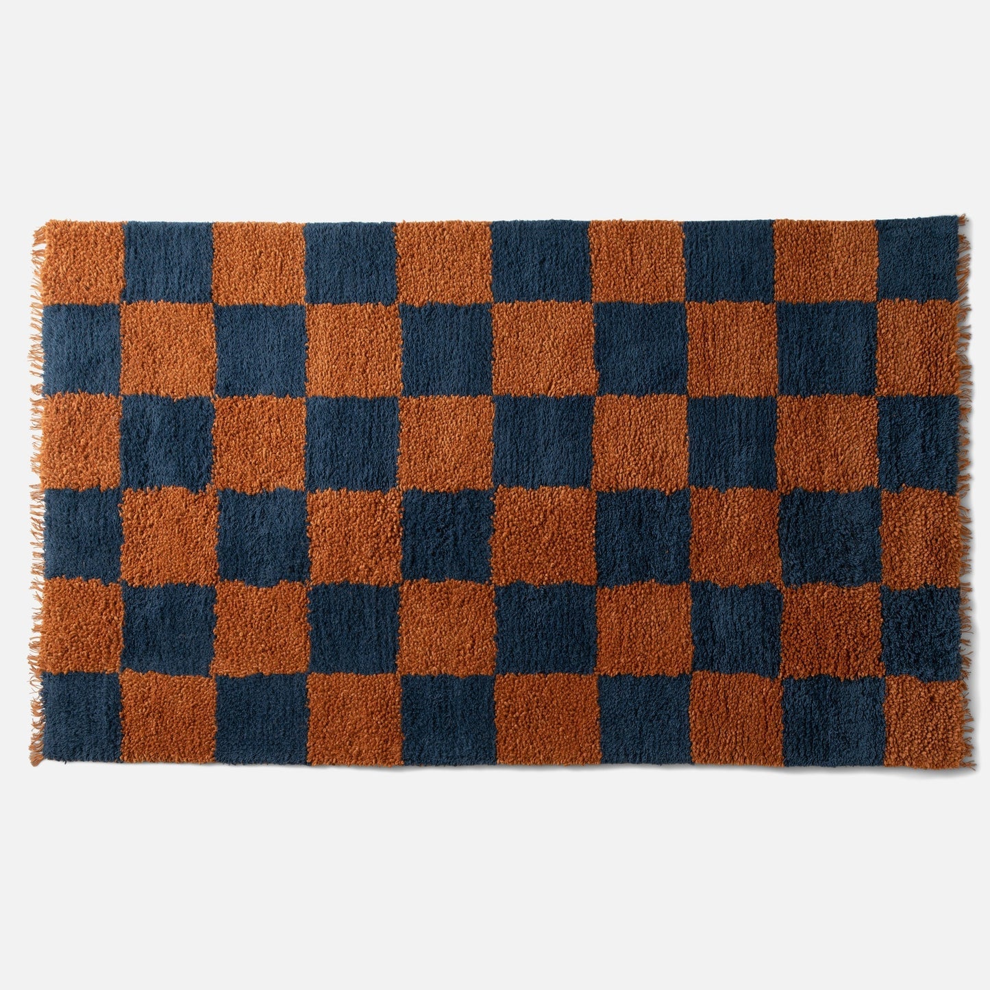 Top edge of Jacques shag wool rug showing rust and navy checked high-pile wool, visible fringe on white background