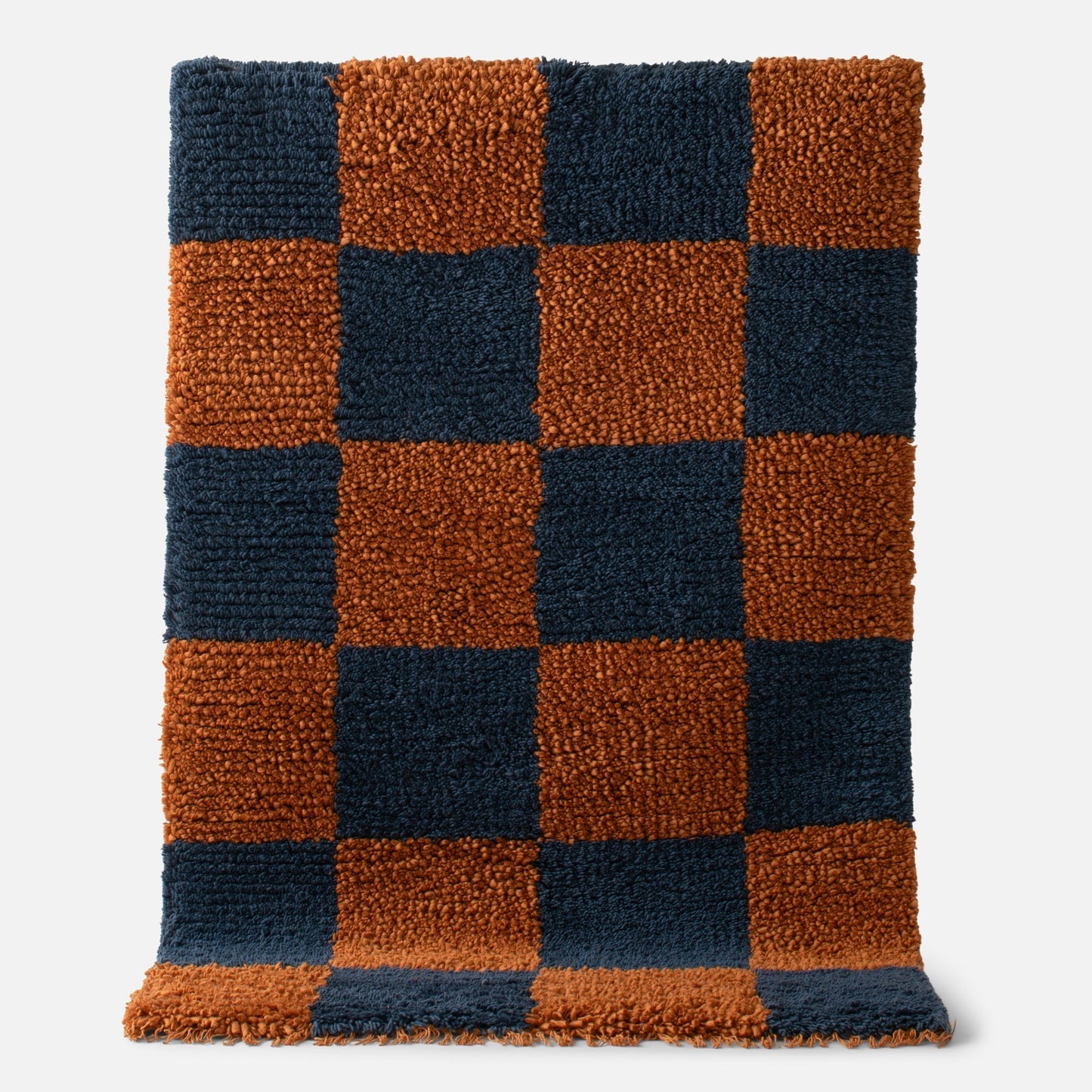 Close-up of Schoolhouse x Clare V Jacques shag wool rug showing navy and rust checkerboard with fringe