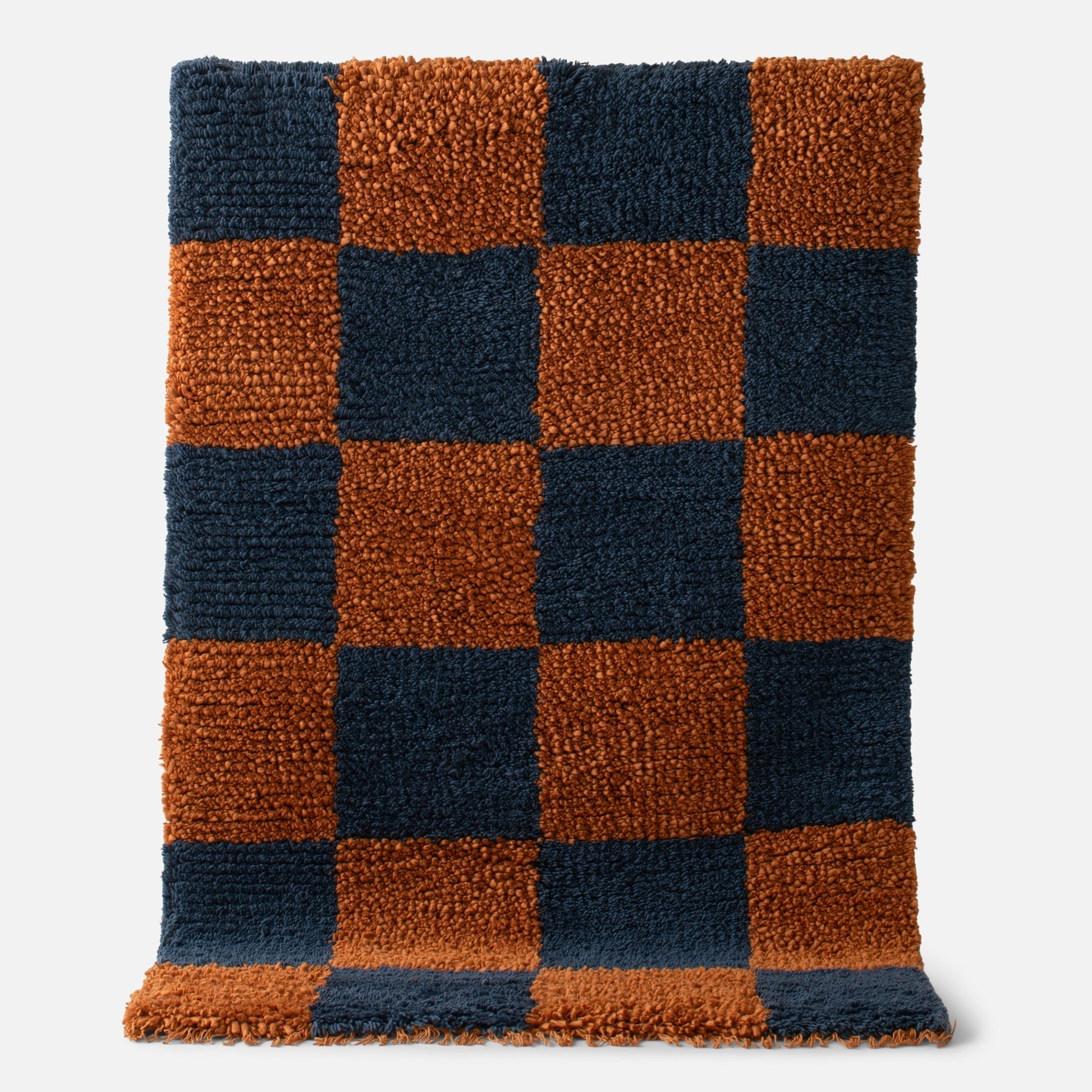 Close-up of Schoolhouse x Clare V Jacques shag wool rug showing navy and rust checkerboard with fringe