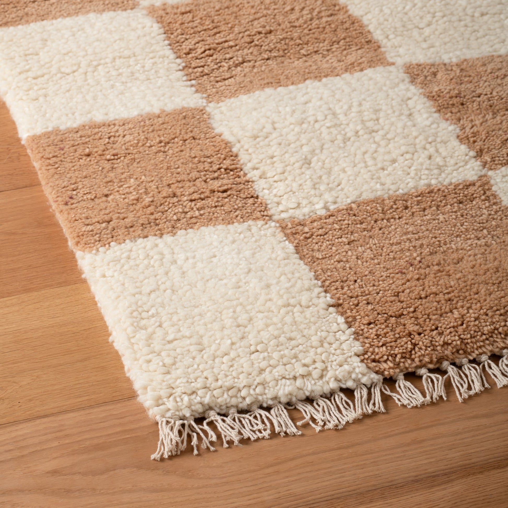 Close-up of Schoolhouse x Clare V. Jacques Shag Wool rug showing cream and tan check pattern, high-pile wool texture and fringe on wood floor