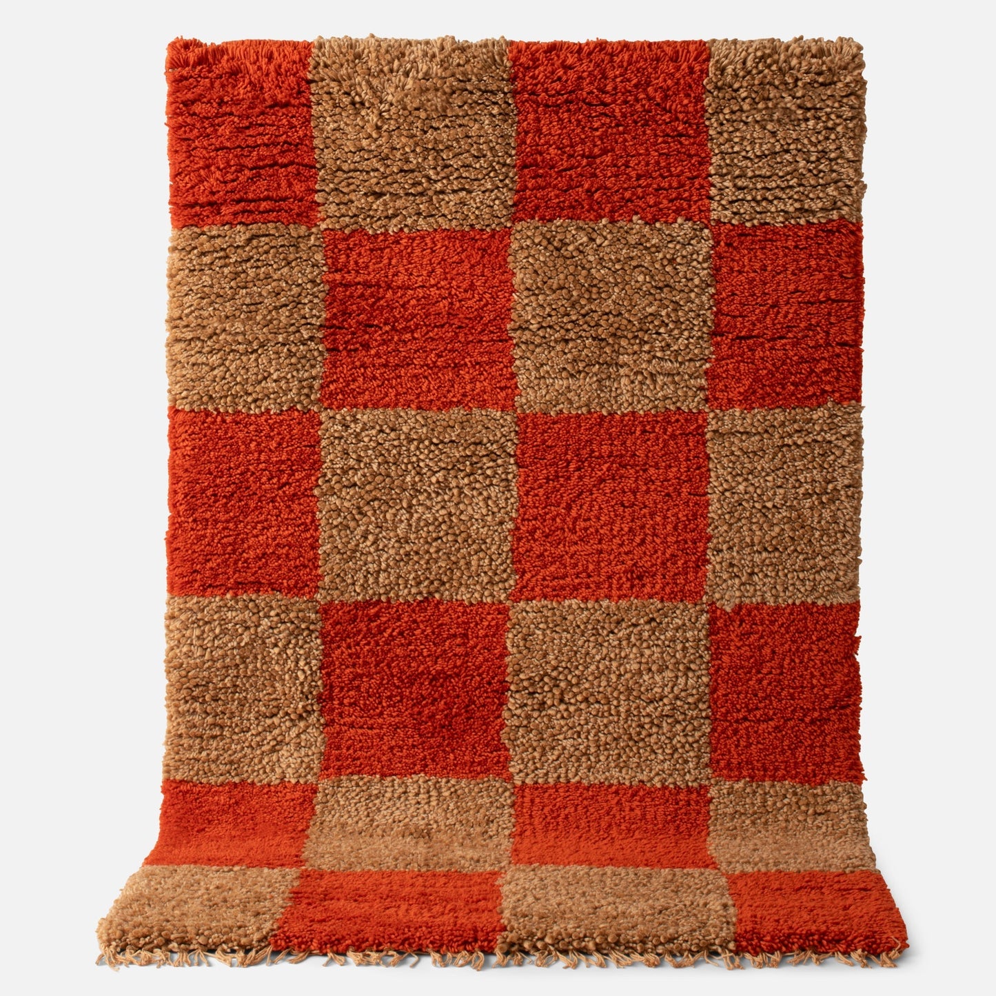 Top view of Schoolhouse x Clare V Jacques Jacques shag wool rug showing persimmon and tan checkerboard high-pile wool with fringe on white background