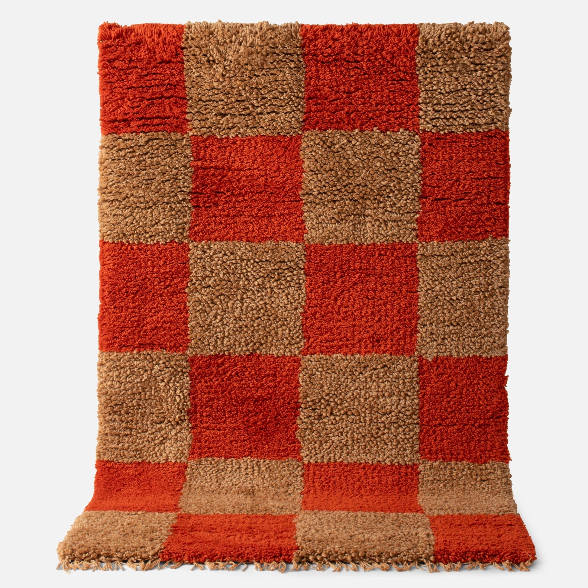 Top view of Schoolhouse x Clare V Jacques Jacques shag wool rug showing persimmon and tan checkerboard high-pile wool with fringe on white background