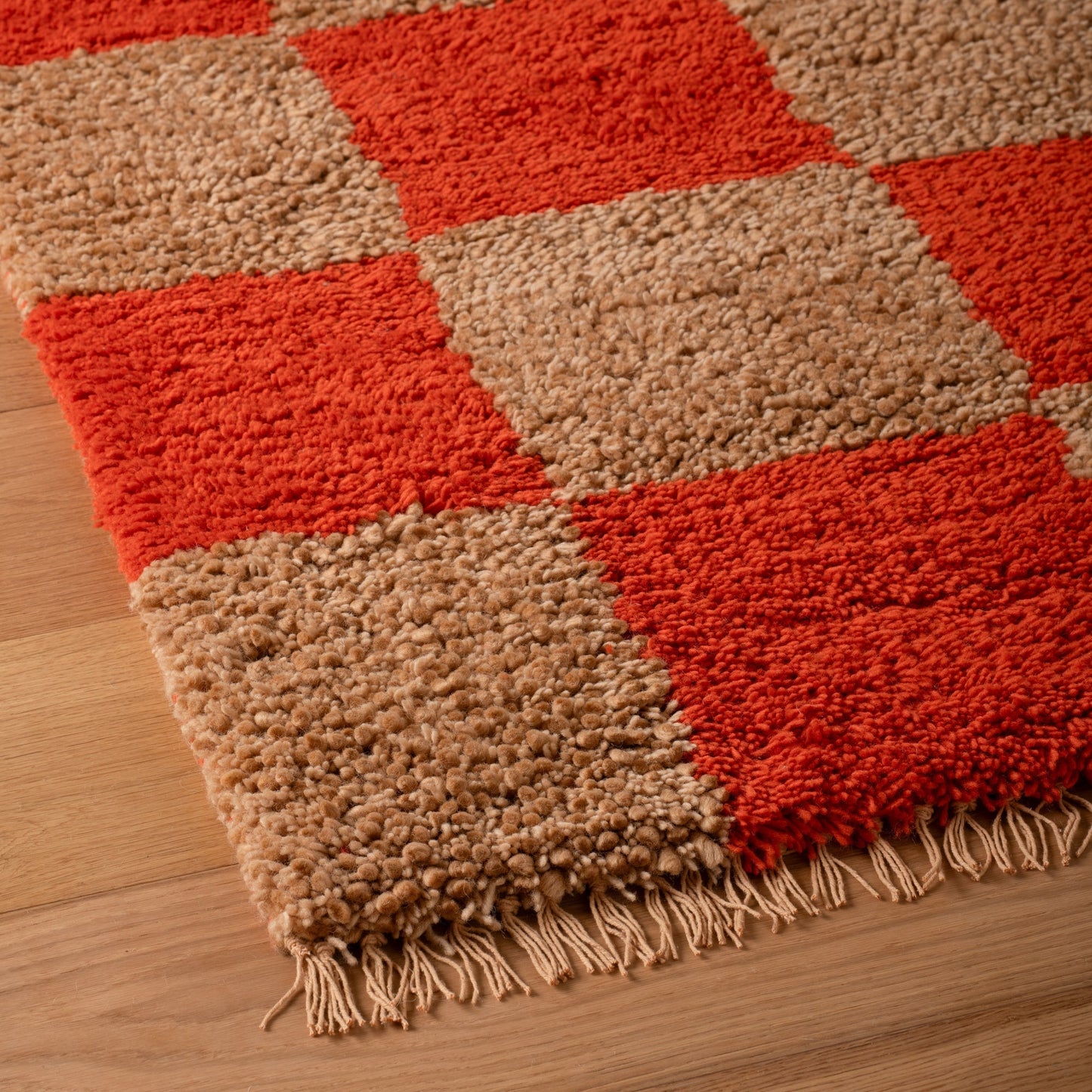 Close-up of Jacques Shag Wool Rug showing high-pile wool shag, bold persimmon and cream checks and fringe on wood floor